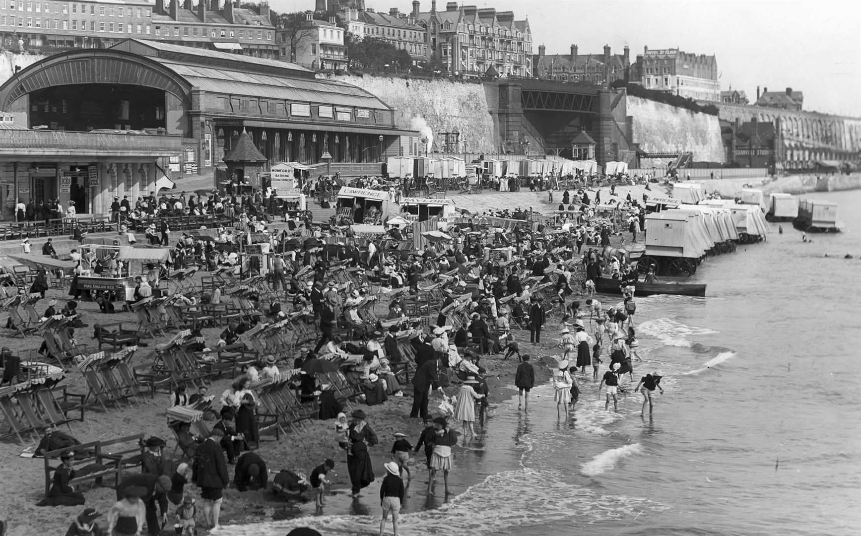 The old Ramsgate Harbour station looms in the background as people pack the beach with deck chairs